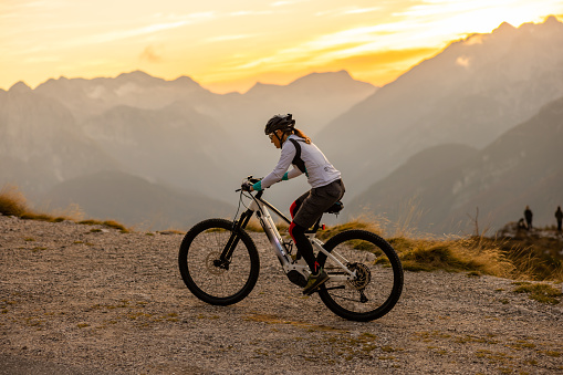 Woman with long brown hair tied in a ponytail,wearing sunglasses,a helmet and sports clothing with a shorts riding up the Mangart mountain,side view