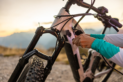 Close-up woman with sports clothing charging her e-bike with a cable during sunrise on a mountain