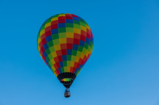 Rainbow checkered hot air balloon isolated on clear blue sky,view from the side people standing in the basked underneath the balloon