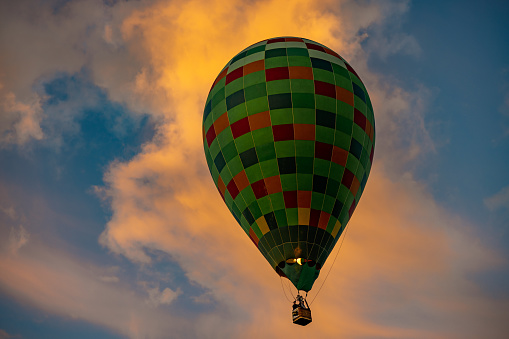 Green teardrop shaped hot air balloon soaring trough the sky,cloud in the background during sunrise