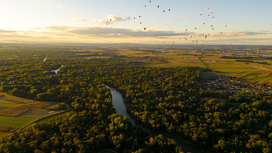 Beautiful aerial view of a landscape with lots of hot air balloons soaring in the sky during sunrise,river with forest in the front