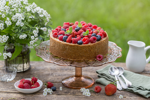 cheesecake with summer berries on wooden table in garden, rustic style, picnic outdoor, selective focus