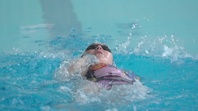 Young woman, a professional swimmer, swims in a backstroke style.
