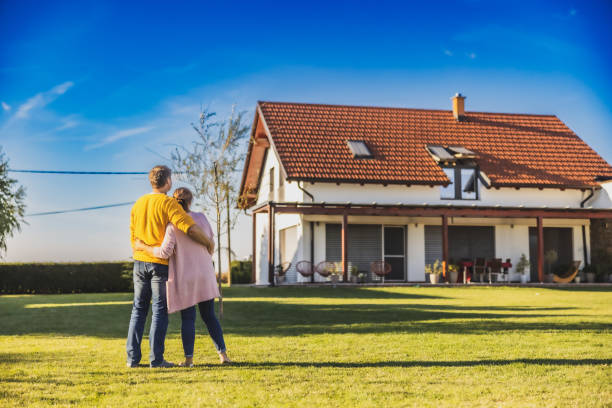 Couple,man and woman,hugging each other while standing on the lawn in the backyard of their new bought house,rear view,modern house in the background Couple,man with short brown hair and woman with long brown hair,hugging each other while standing on the lawn in the backyard of their new bought house,rear view,modern house in the background with almost clear sky in the evening House to Buy stock pictures, royalty-free photos & images
