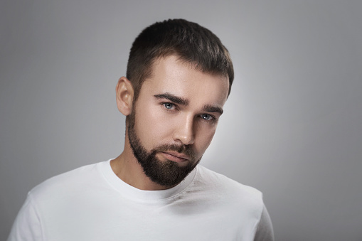 Portrait of young and handsome bearded  man with clean skin against gray background