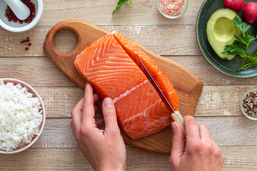 famale hands cutting raw salmon fillet on wooden board, top view