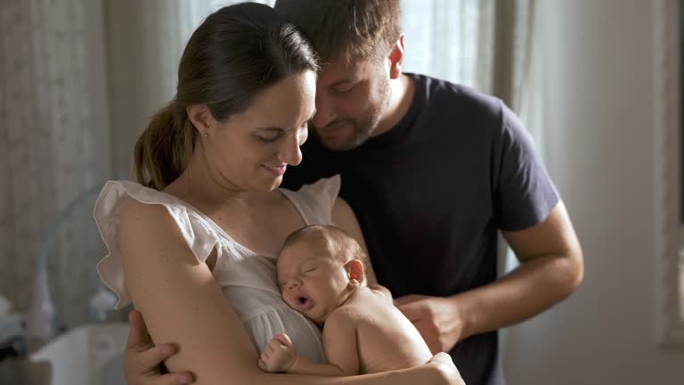 Loving Family Portrait: Young Couple Embracing their New Born Baby and Looking at him With Love. Gentle Moment Shared between a Married Man and Woman as they Become Parents. Slow Motion Shot