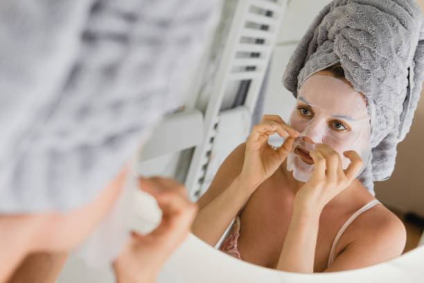 istock Woman in bathroom with applied sheet mask on her face looking in the mirror 1466682811