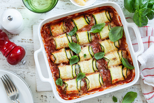 stuffed zucchini rolls with tomato sauce in white baking dish, top view