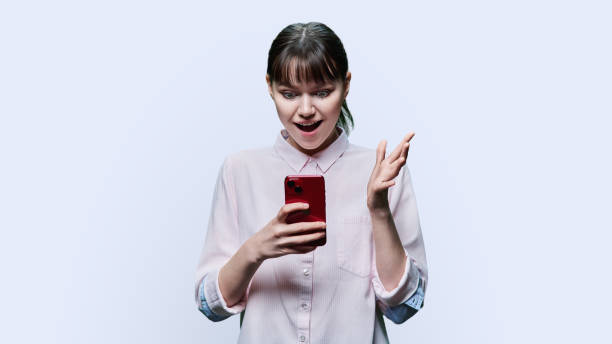 istock Surprised young female looking at smartphone on white background 1466687398