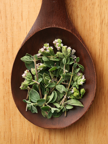 Top view of wooden spoon with fresh oregano leaves and flowers on it