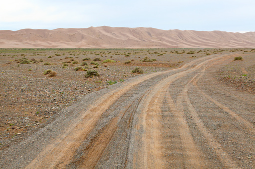 View of tire track on empty dirt road passing through Gobi desert, Khongoryn Els, Gobi Gurvansaikhan National Park, Mongolia.