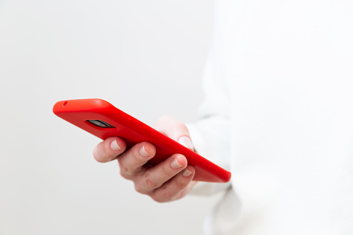 Close up of woman's hand using, holding smartphone in red phone case on white background. Copy space.