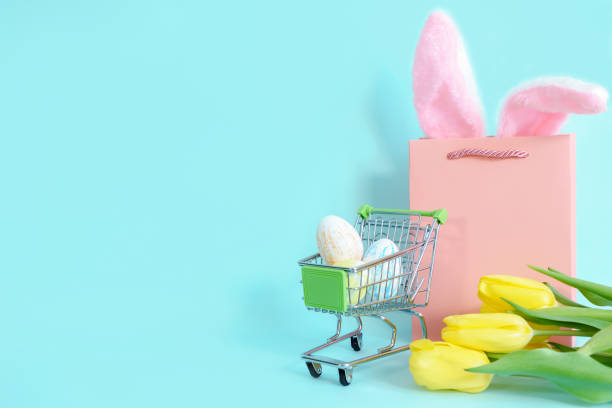 istock Easter eggs in a grocery basket on a blue background with yellow tulips and rabbit ears in a paper bag. easter, shopping 1466695122
