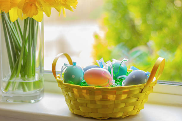 istock yellow basket with Easter colorful eggs on window sill with flowers. 1466699618