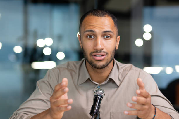 Closeup portrait man with a professional microphone, African American recording audio and video podcast sitting in the studio, call of a serious businessman talking and chatting with colleagues Closeup portrait man with a professional microphone, African American recording audio and video podcast sitting in the studio, call of a serious businessman talking and chatting with colleagues. speaker of the house stock pictures, royalty-free photos & images