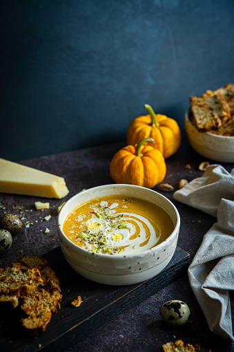 Homemade pumpkin soup with quail egg, sour cream, parmesan and pistachios and homemade savory biscotti with sun dried tomatoes on dark background.