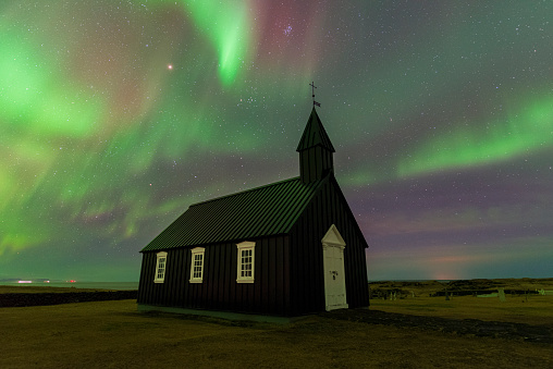 The wooden iconic black church in the starry night under the colors of northern lights, Budir, Vesturland, Iceland