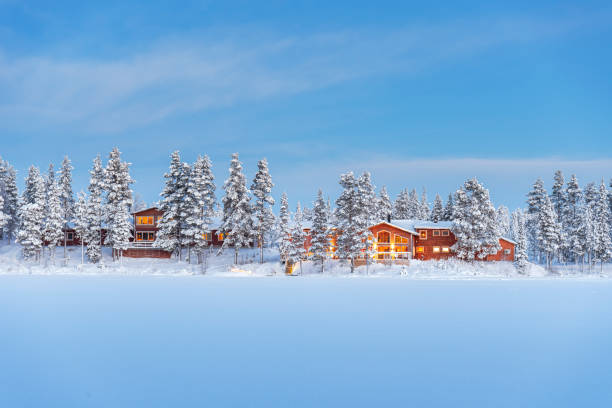 Wooden chalets among snow covered trees, Lapland, Sweden Winter view of illuminated chalets in the frozen coniferous wood covered with snow beside the icy lake, dusk time, Norrbotten, Lapland, Sweden swedish sauna stock pictures, royalty-free photos & images