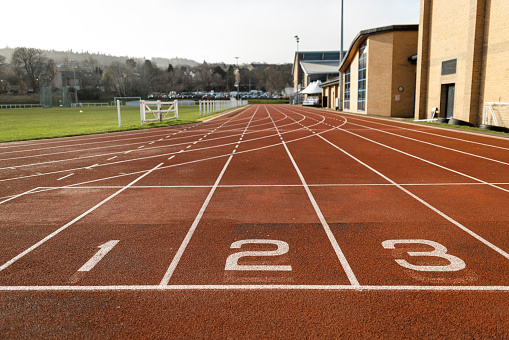 A shot of the start line on running track within a sports facility. The track is empty on a bright sunny day.