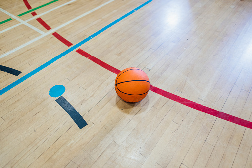 A shot of a single basketball resting on the floor in an indoor basket ball court. There are no people in the shot