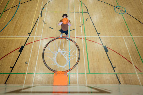 Shooting a Basketball A wide angle shot of a male teenage amputee playing basketball. He has a bionic leg and is taking a shot. The photo is taken from behind the net and is looking down onto him. college basketball court stock pictures, royalty-free photos & images
