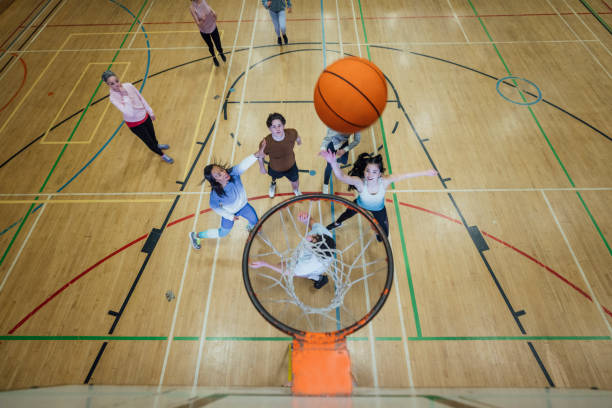 Basketball Game A shot of a diverse group of teenagers playing basketball. The shot is taken from behind the basketball net looking down onto the players. The basketball is in mid motion as someone takes a shot. youth basketball indoor stock pictures, royalty-free photos & images
