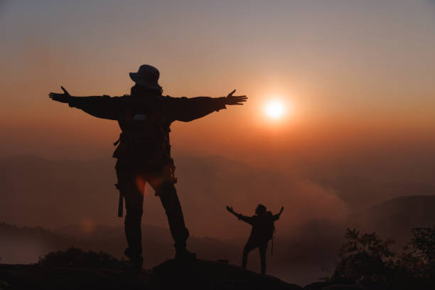 widok z tyłu mężczyzny i kobiety na skale podnieś rękę, aby pokazać sukces na klifie - mountain cliff mountain peak plateau zdjęcia i obrazy z banku zdjęć