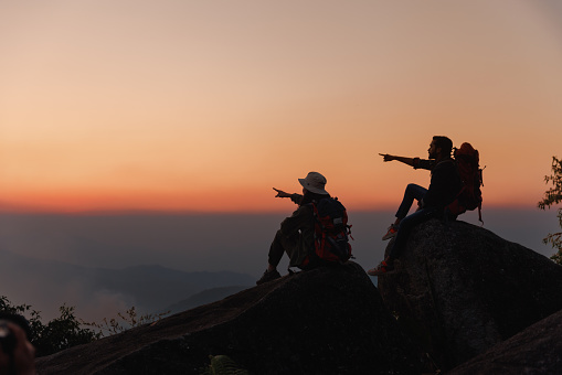 Adventure Man and woman sitting on the peak and pointing to the horizon