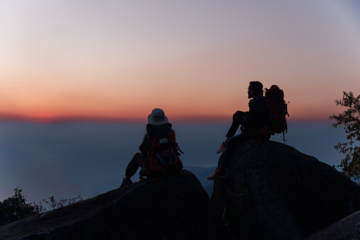 Rear View Of adventure Man and woman On Rock sitting on the peak and see sunset on evening