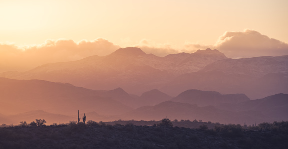 Sunrise with saguaro cactus silhouettes and snow-covered Superstition Mountains in the distance