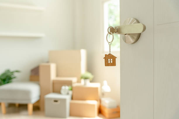 mudança de casa, realocação. a chave foi inserida na porta da nova casa, dentro do quarto havia uma caixa de papelão contendo pertences pessoais e móveis. mudança no apartamento ou condomínio - key house home interior key ring - fotografias e filmes do acervo