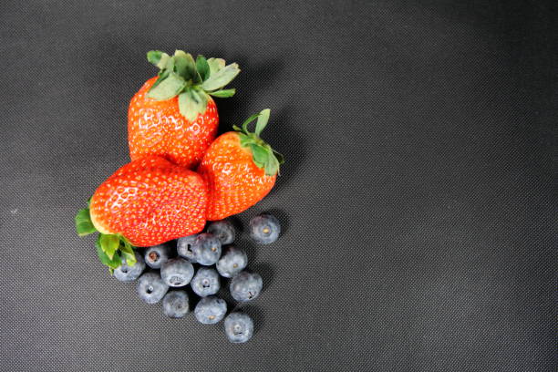 Group of strawberries and blueberries. The fruit is on the left side, the right side is empty. The background is black.