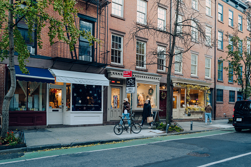 New York, USA - November 21, 2022: Row of shops on a street in West Village, a charming area of Manhattan famous for its shops and restaurants, women walking past.