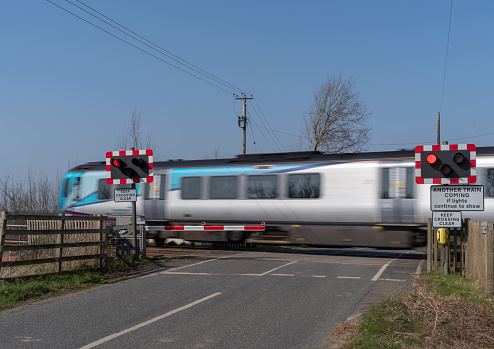 24 March 2022 - A moving train passing over an automatic half barrier level crossing on clear day with blue sky.