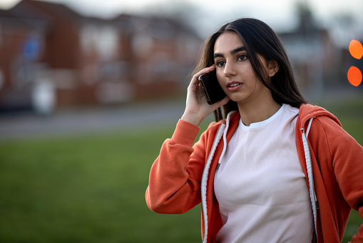 Waist-up shot of a female teenager on her mobile phone. She has a serious expression on her face wearing casual clothing.