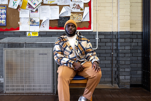 A full shot of a young adult sitting in casual clothing looking at the camera in a community centre. He has a negative emotion on his face. The community centre is located in Seaton Deleval in the North East of England.