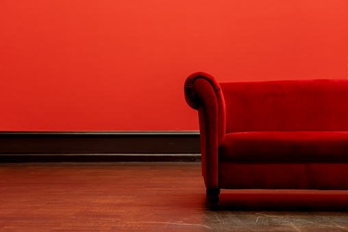 Half of a red sofa in a reading room with wooden floors.