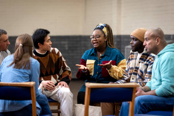 Explaining To the Group in Community Centre Medium shot of a group of adults sitting in a circle and talking to each other about their mental well-being. They are all wearing casual clothing. The community centre is located in Seaton Deleval in the North East of England. social interaction stock pictures, royalty-free photos & images