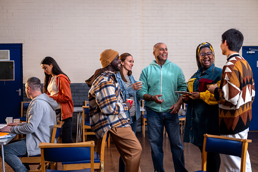 Three-quarter-length shot of a group of adults standing in a circle and talking to each other about their mental well-being. There is a staff member sitting to the left of them in the frame sitting next to a table. The community centre is located in Seaton Deleval in the North East of England.