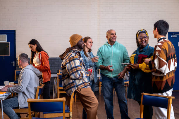Catching Up with Friends at The Community Centre Three-quarter-length shot of a group of adults standing in a circle and talking to each other about their mental well-being. There is a staff member sitting to the left of them in the frame sitting next to a table. The community centre is located in Seaton Deleval in the North East of England. social interaction stock pictures, royalty-free photos & images