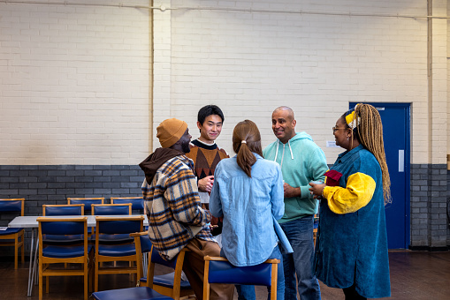 Three-quarter-length shot of a group of adults standing in a circle and talking to each other about their mental well-being. They are all wearing casual clothing. The community centre is located in Seaton Deleval in the North East of England.