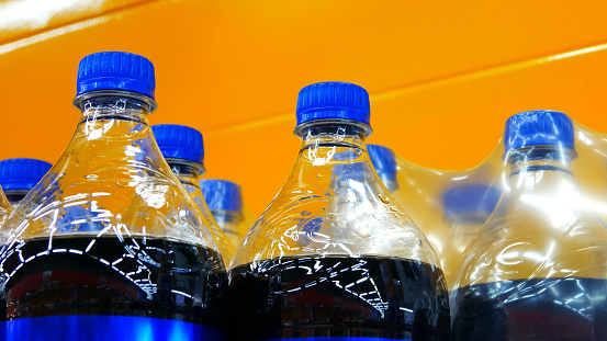 Many plastic bottles with cola against yellow background close-up