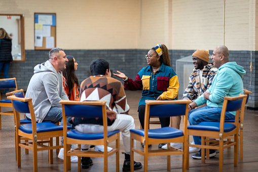 Full shot of a group of adults sitting in a circle and talking to each other about their mental well-being. They are all wearing casual clothing. The community centre is located in Seaton Deleval in the North East of England.