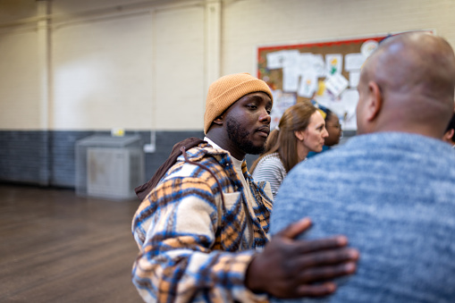 A waist-up shot of a male adult with his hand on an unrecognisable person's shoulder in a community mental health discussion group. The community centre is located in Seaton Deleval in the North East of England.