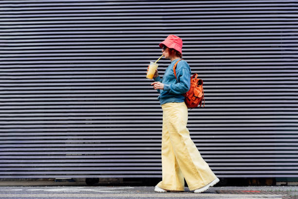 istock Stylish girl in bright clothes drinking sugar flavored tapioca bubble tea while walking near gray striped urban wall. Full length portrait of fashionable hipster girl. Street fashion. Copy space. 1466738304