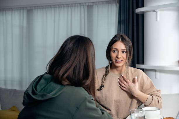 Younger sister visiting her older sister in her new apartment she moved into after divorcing her abusive ex-husband. Two women sitting and talking at the kitchen counter drinking coffee and enjoy stock photo