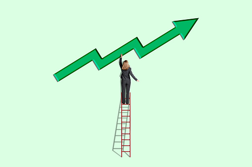 A woman standing on a ladder reaches. up for a large green arrow that points in a positive, upward direction.