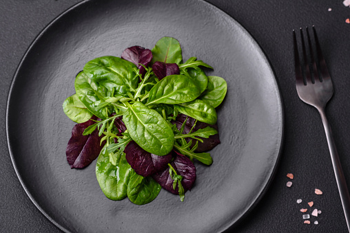 Delicious fresh salad consisting of spinach, chard, radicchio, red chart, bulls blood and arugula on a black plate on a dark concrete background
