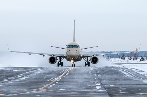 Front view of the passenger airplane taxiing on taxiway in snowy winter day